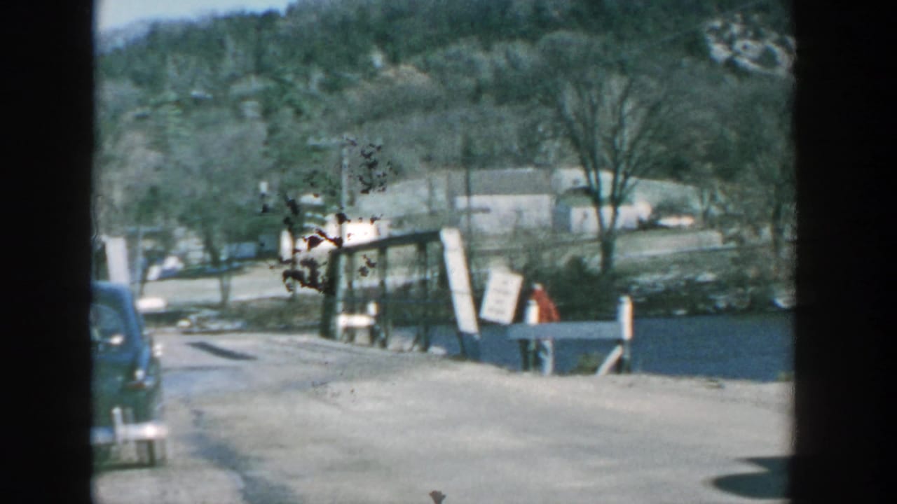 Road by a small bridge with a dark vintage car partly visible and water to the side.