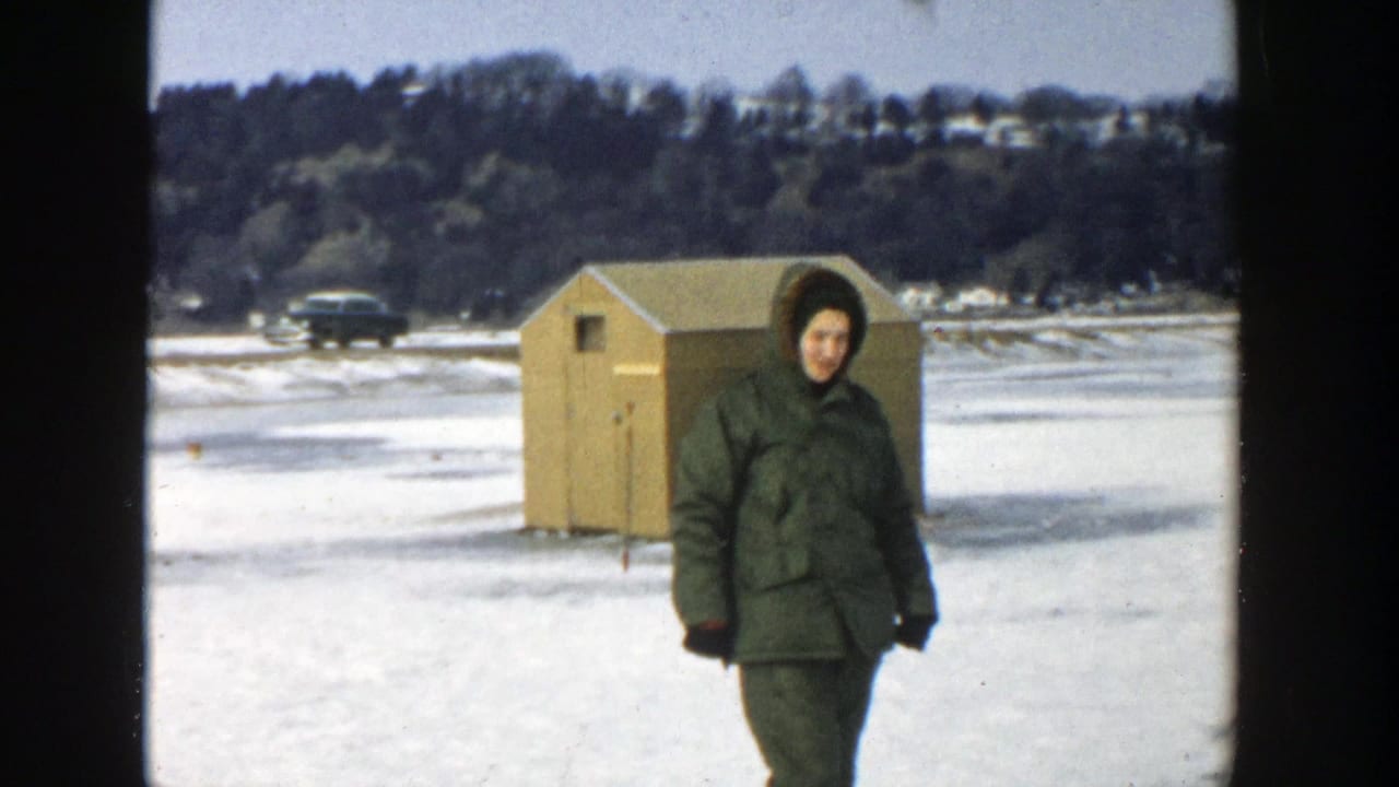 Woman in winter clothing walking past a wooden shelter on the ice.