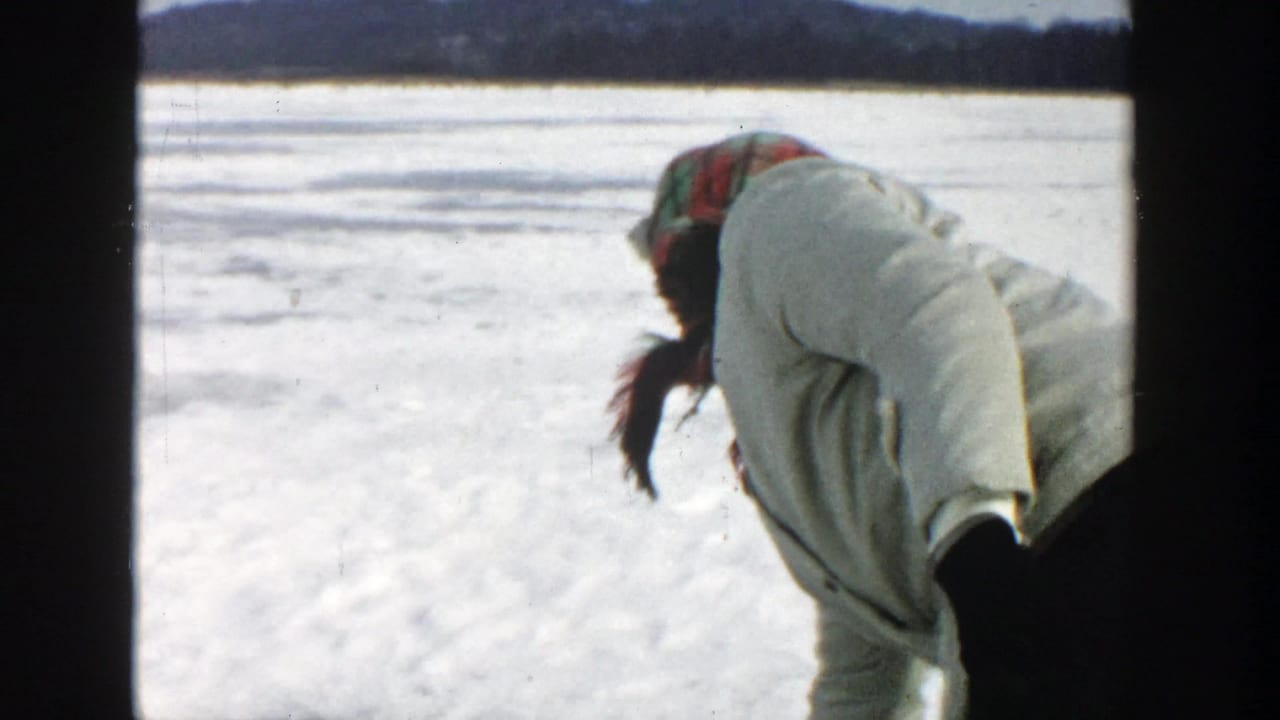 Woman in a white coat and red headscarf leans forward on a frozen lake.