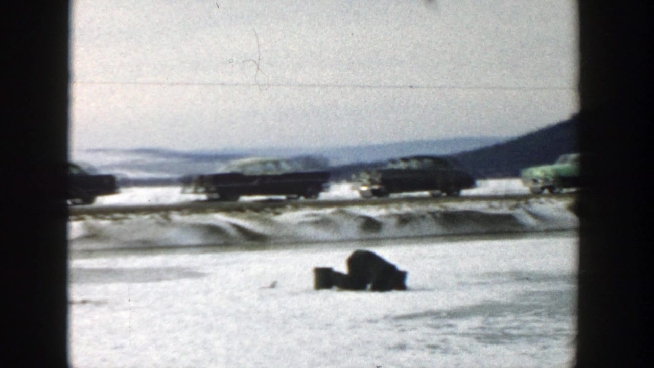 Snowy roadside with cars in the background and a dark object in the foreground.