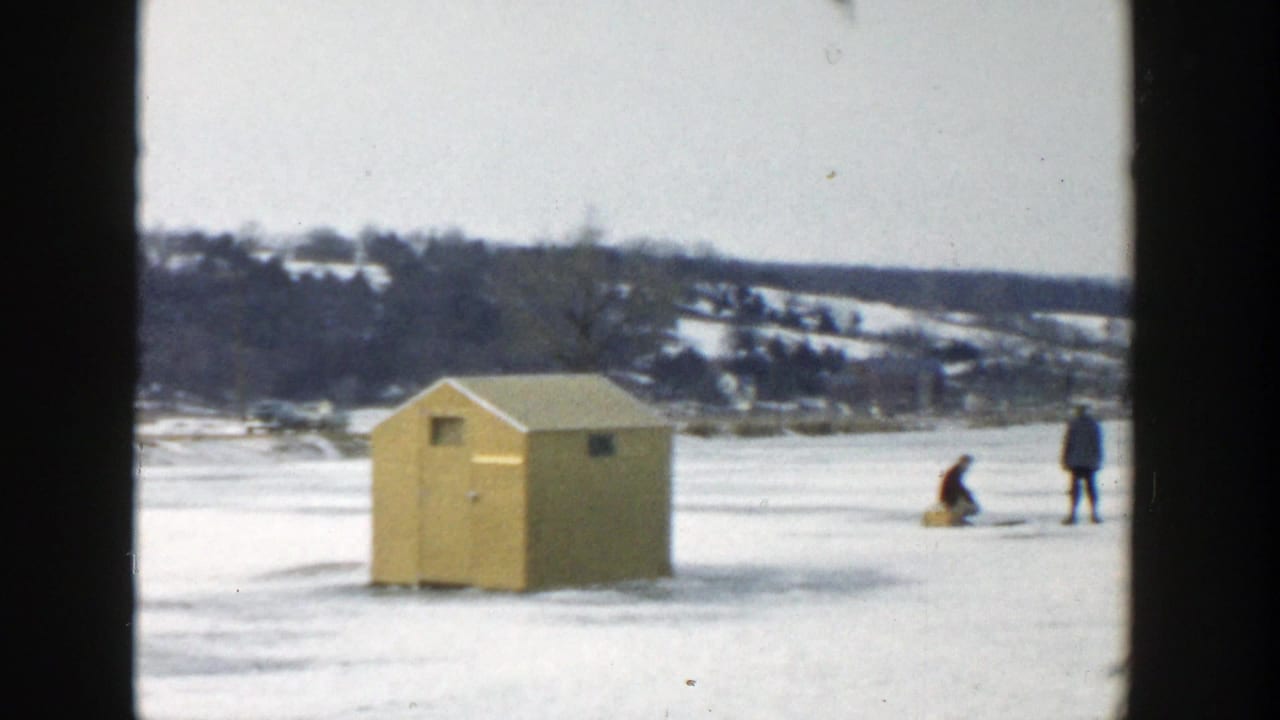 Yellow ice-fishing hut with two distant people on the frozen lake.