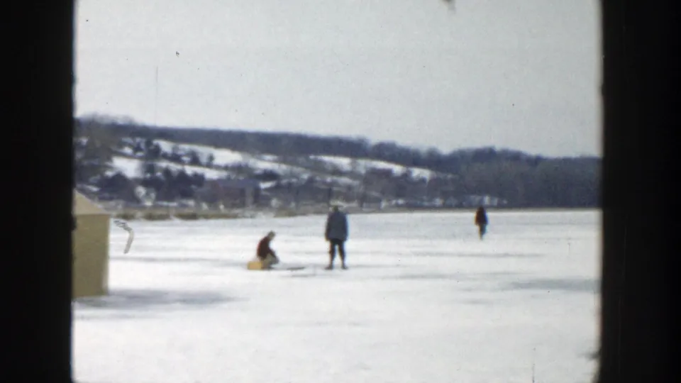1957 Wisconsin 8mm frame with two figures near an ice-fishing spot and another person farther across the frozen lake.