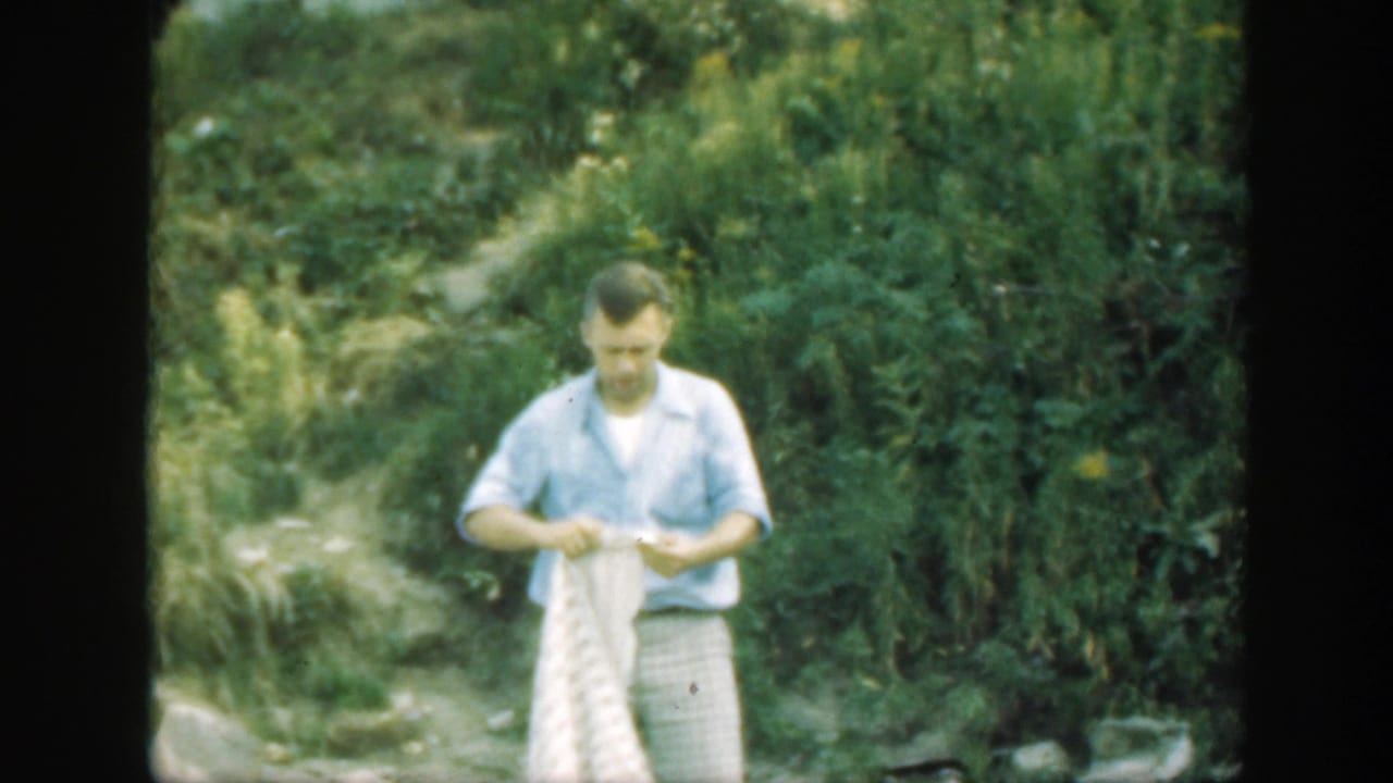 Man standing outdoors while beginning to fold a white textured sheet.