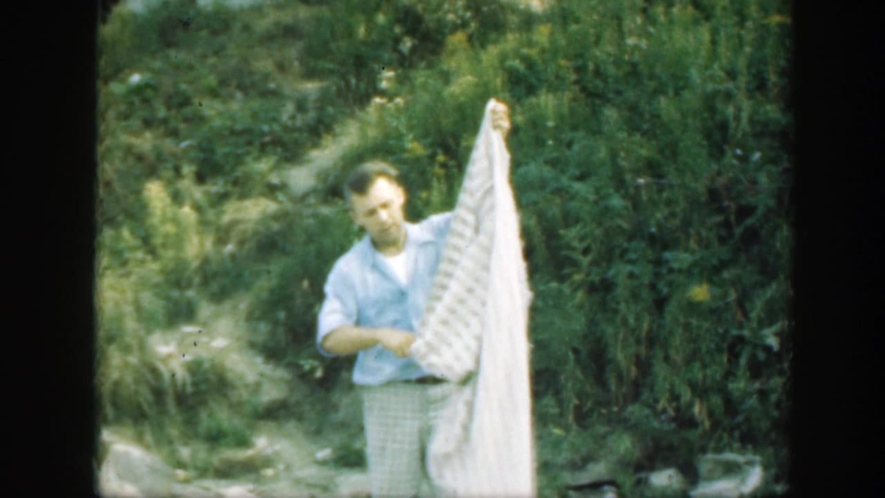Man outdoors lifting one side of a white patterned sheet.