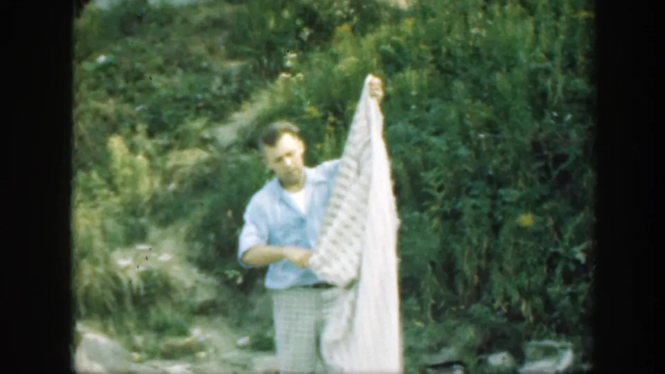The man raises part of the white patterned sheet in a green outdoor Connecticut setting documented as 1947.