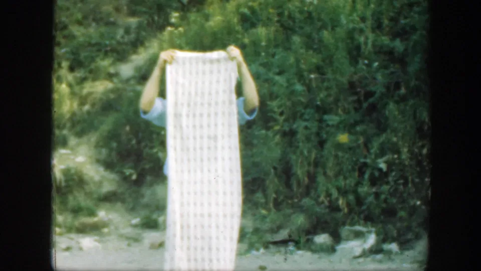 The man holds the white textured sheet upright, nearly covering his face, in 1947 Connecticut outdoor home-movie footage.