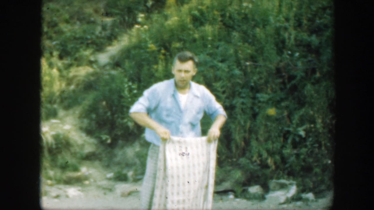The man faces forward in a Connecticut wooded area, holding a pale checkered blanket at waist height.