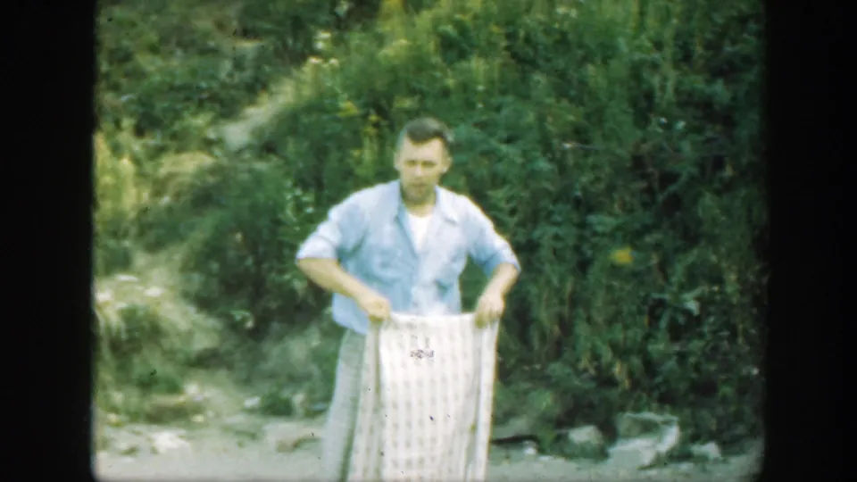 The man faces forward in a Connecticut wooded area, holding a pale checkered blanket at waist height.