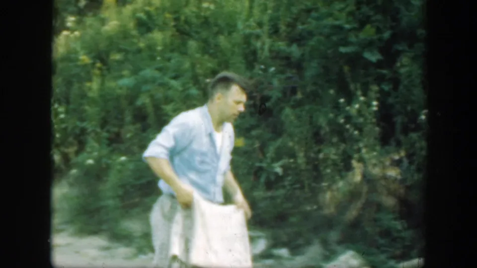 A man in patterned trousers bends over the blanket in a wooded Connecticut setting from the 1947 home movie.