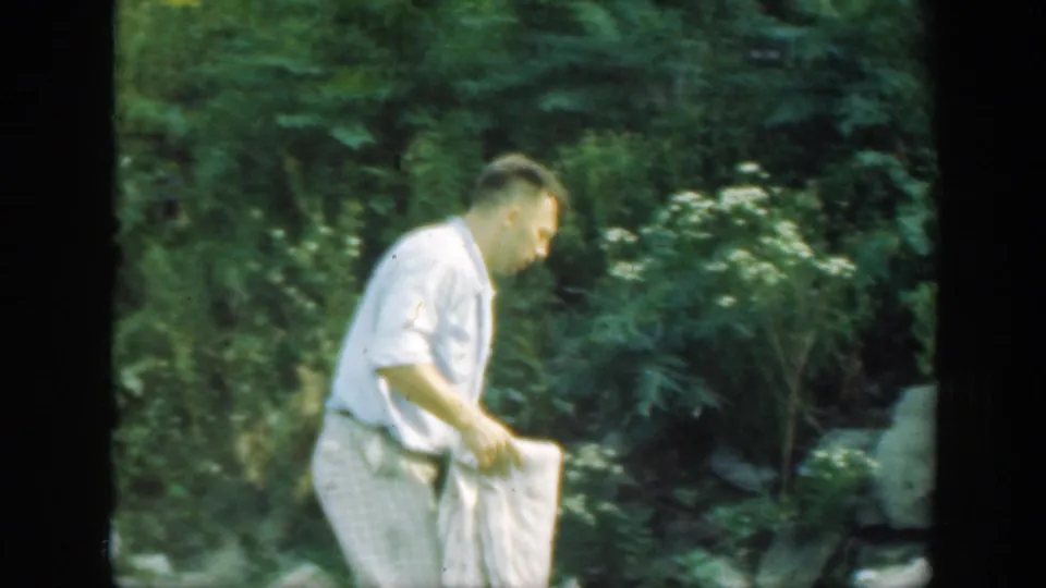 The man moves in profile through the Connecticut woods, carrying the pale checkered blanket at his side.
