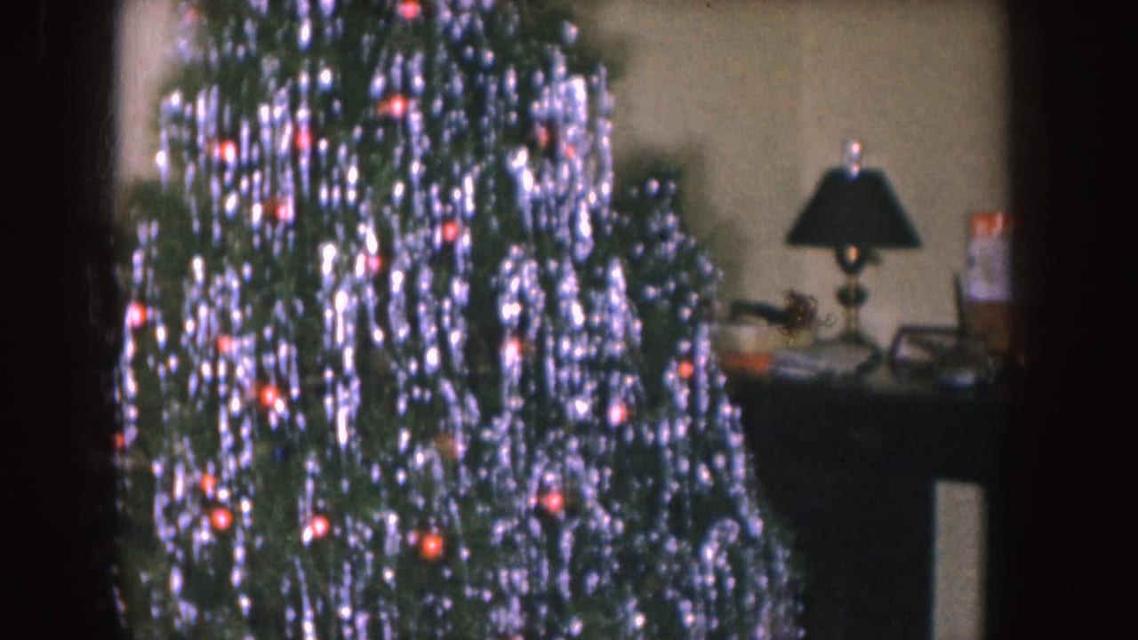 Decorated Christmas tree with silver tinsel, red ornaments, and a nearby table lamp.