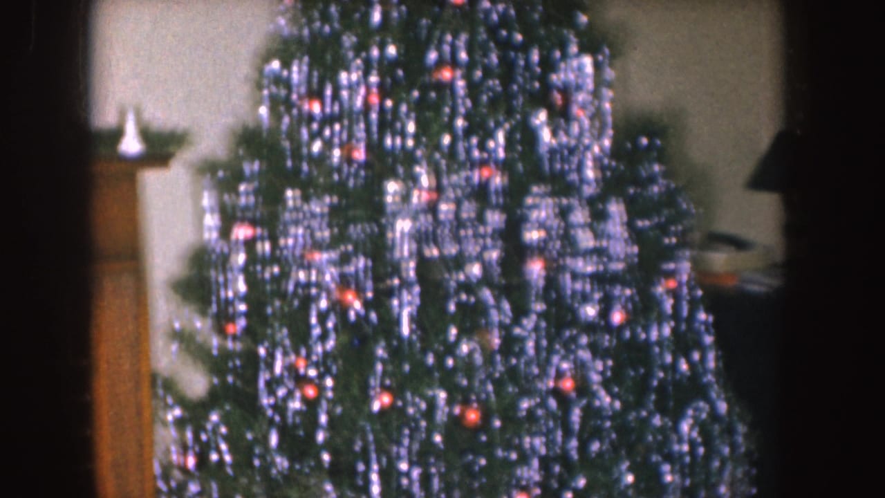 Christmas tree with heavy silver tinsel and red ornaments near a fireplace mantel.