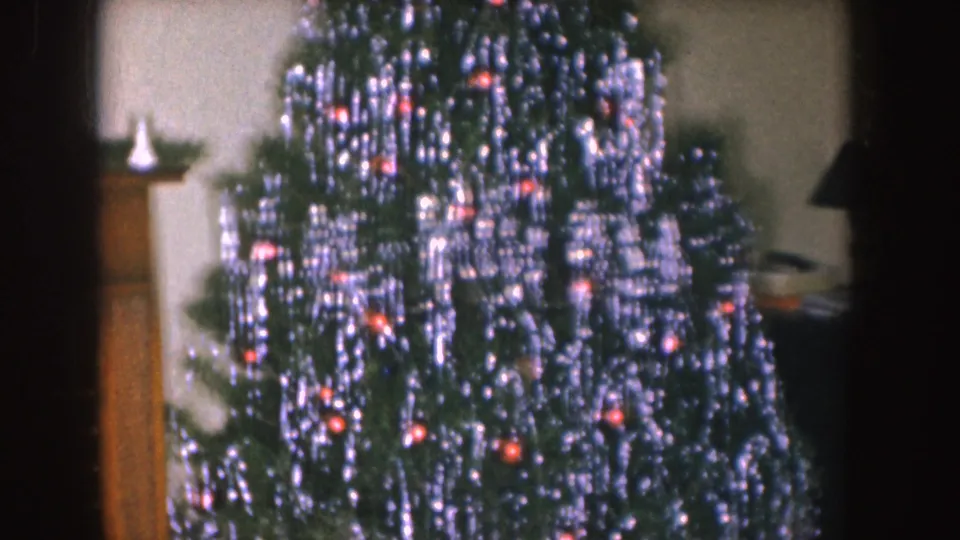 1955 Nebraska interior view of a decorated Christmas tree next to a mantel area with holiday greenery partially visible.