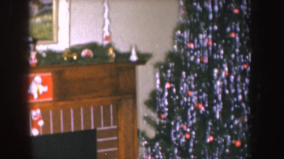 1955 Nebraska home interior showing a wood fireplace mantel decorated with greenery, stockings, Santa imagery, and the edge of a tinsel Christmas tree.
