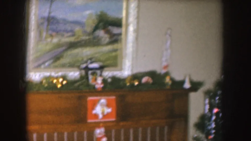 1955 Nebraska interior with a decorated mantel, Santa card, framed landscape painting, candles, and a partial Christmas tree at the right edge.