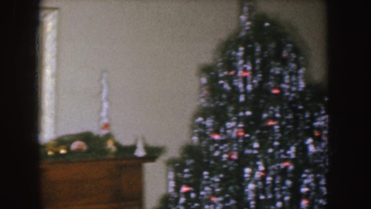 Nebraska 1955 home-movie frame showing a mantel, small holiday objects, and a Christmas tree in a dim living room.