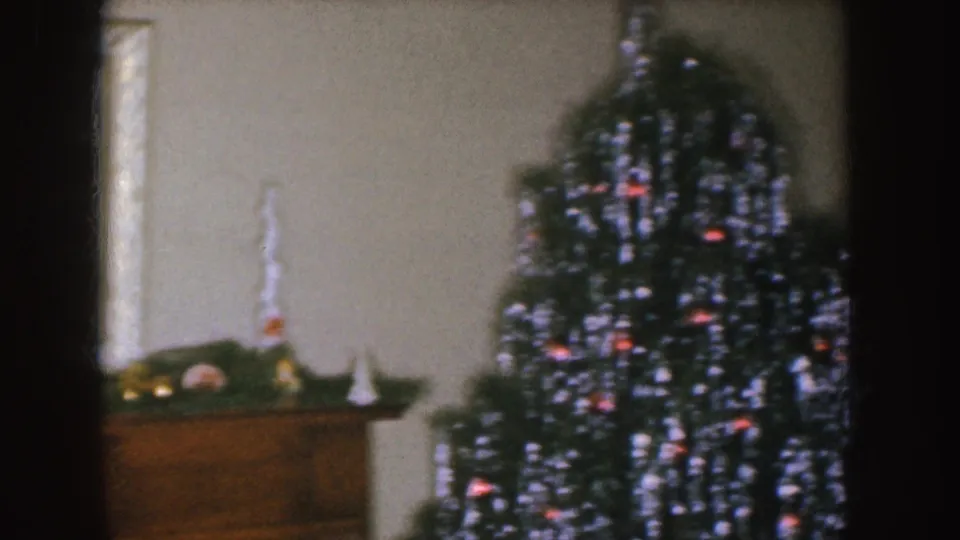Nebraska 1955 home-movie frame showing a mantel, small holiday objects, and a Christmas tree in a dim living room.