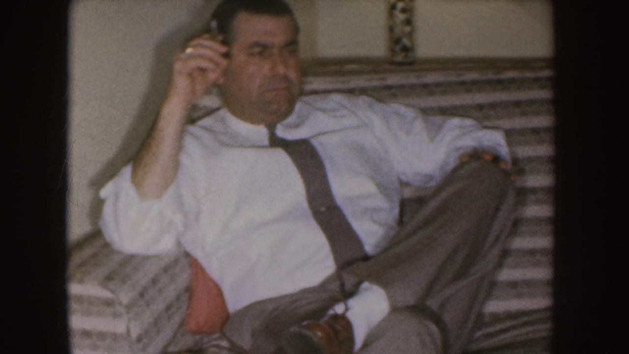 Man reclines on a couch, holding a cigarette with one leg crossed.