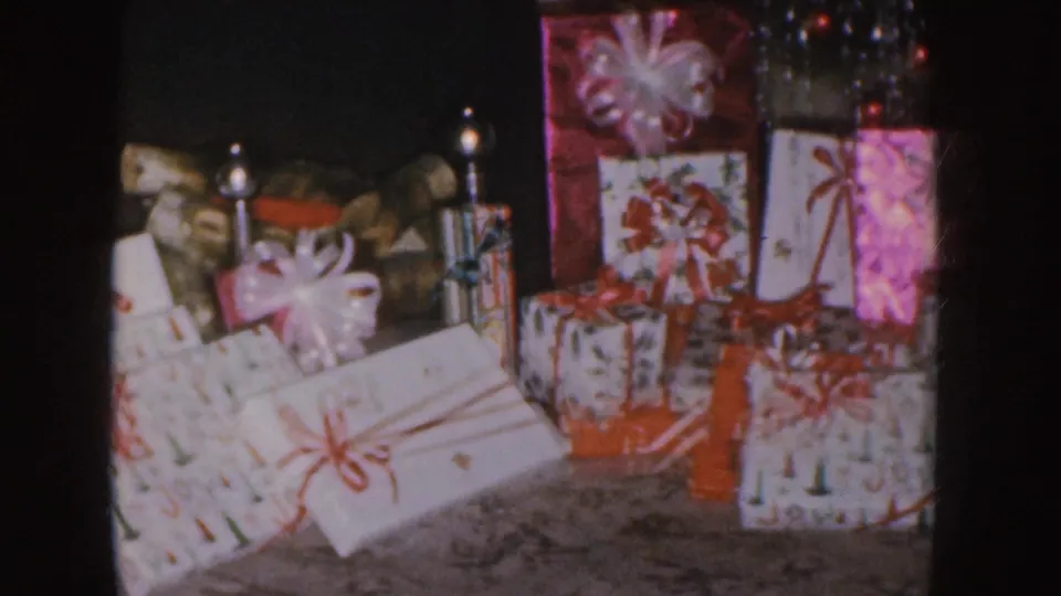 Nebraska 1955 home-movie frame showing wrapped Christmas presents, bows, and tinsel in a room.