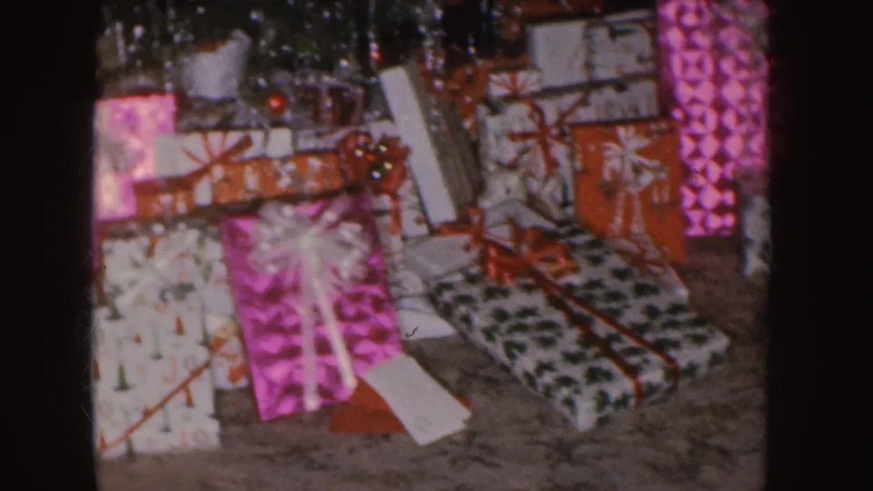 Nebraska 1955 frame showing Christmas gifts, bows, tinsel, and a carpeted room floor.