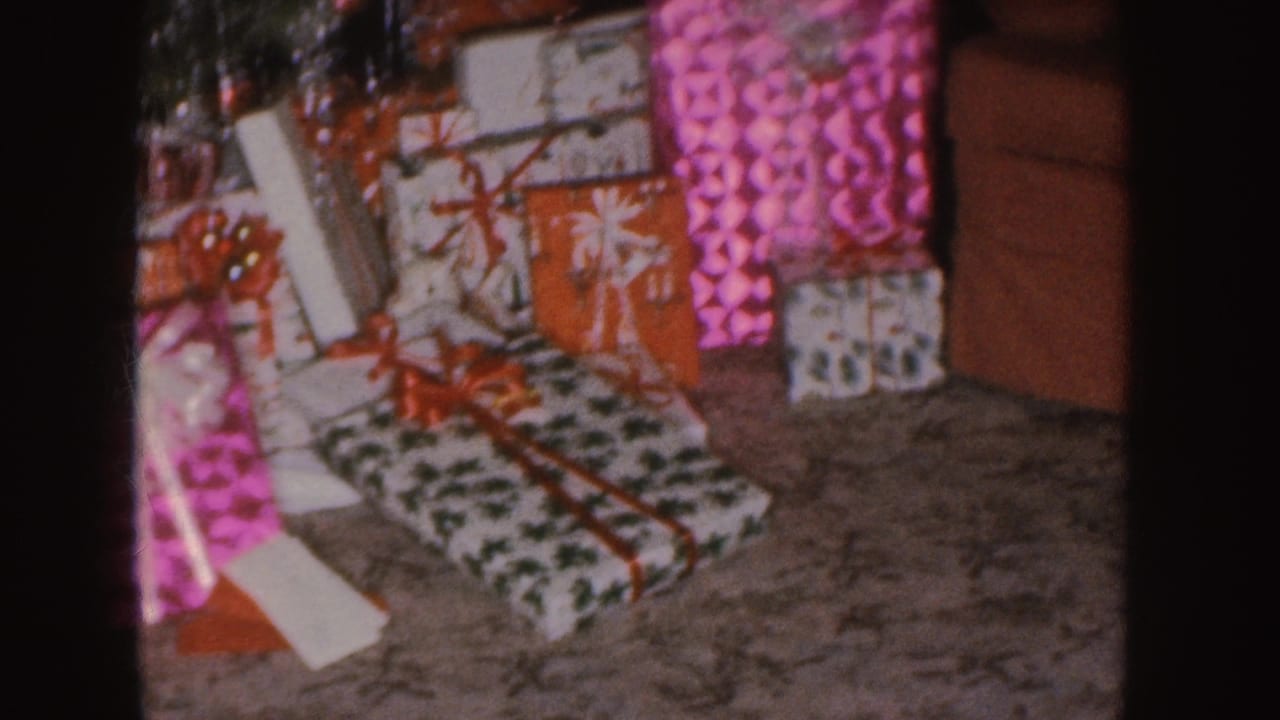 1955 Nebraska 8mm frame showing colorful wrapped Christmas presents beneath a decorated tree in a private living-room interior.