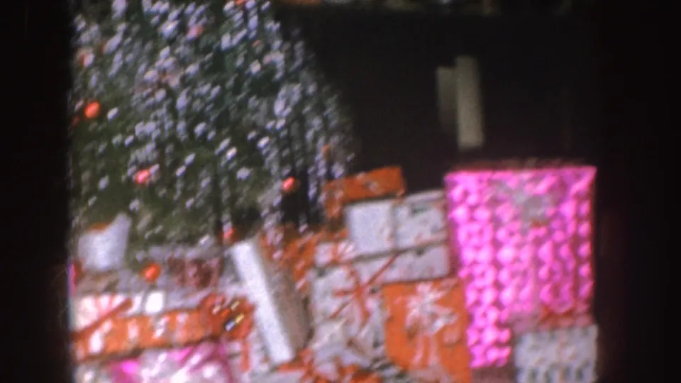 1955 Nebraska 8mm frame showing a decorated Christmas tree with bright wrapped presents in a home living room.