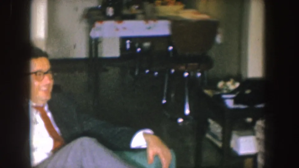 A partly cropped view shows the smiling man beside the couch, with a small table and household items behind him.