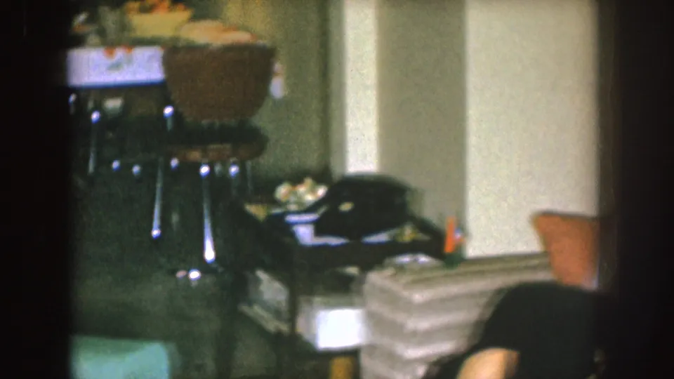 The frame shifts toward the room, showing the couch area, side table, household items and a partial adult at the right edge.