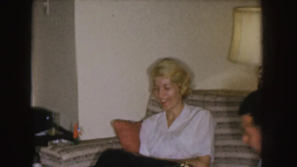 The woman remains seated and smiling on the couch as the man appears partly cropped at the right edge of the frame.