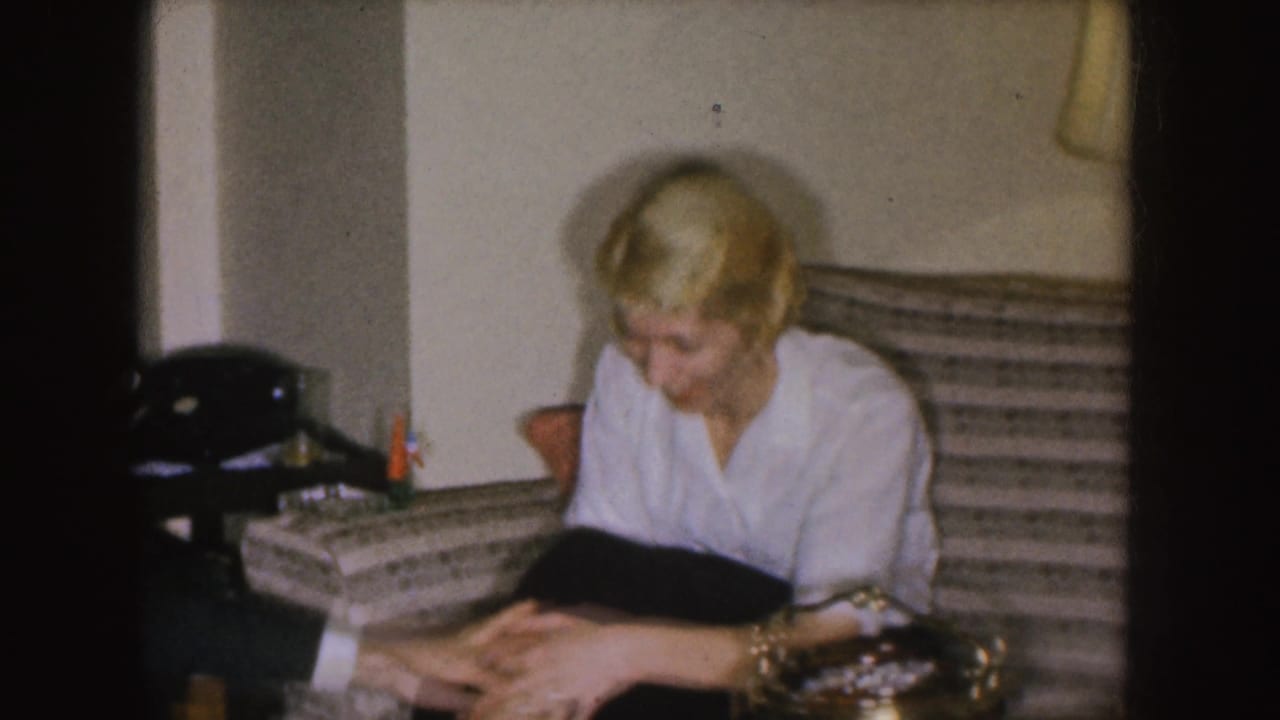 Blonde woman in a white blouse sits on a striped couch and looks down in a living room.
