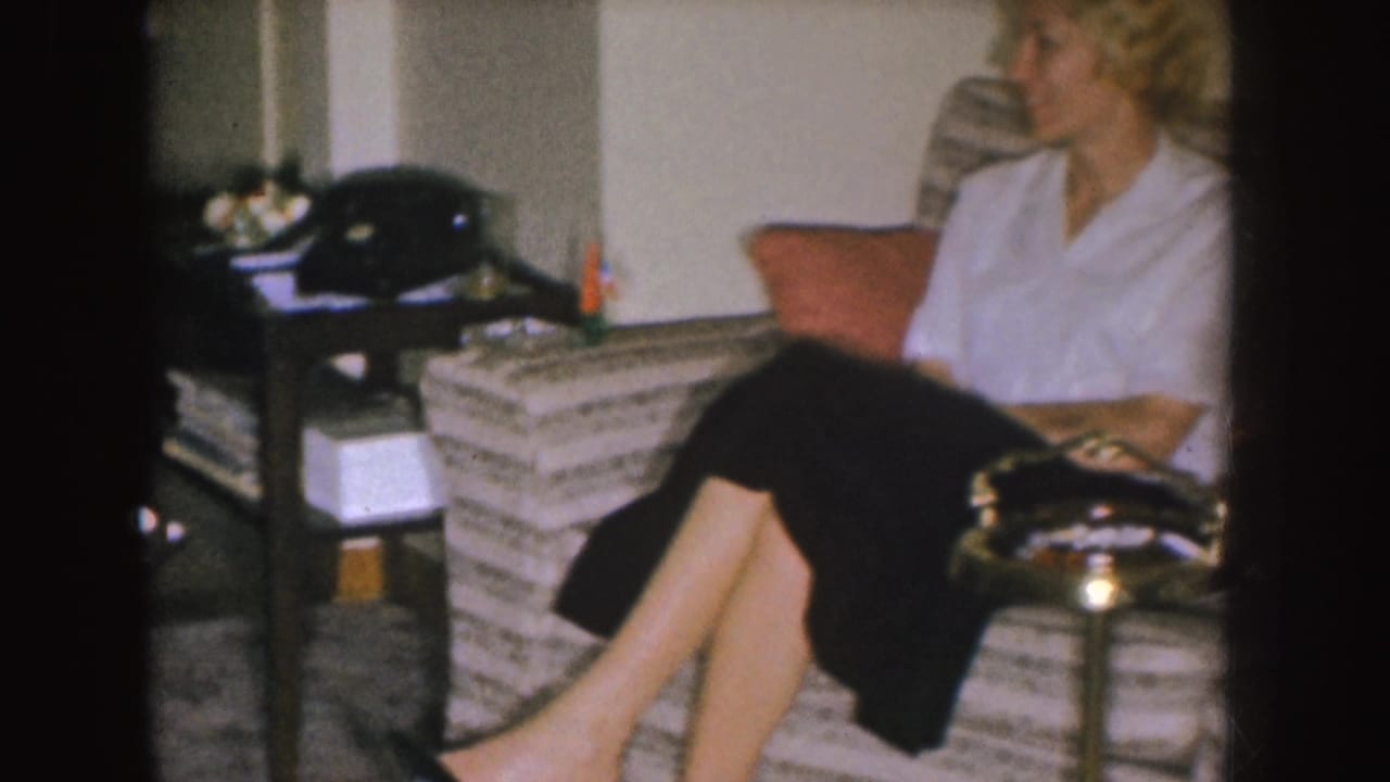 Woman seated on a striped sofa beside a side table with a rotary telephone.