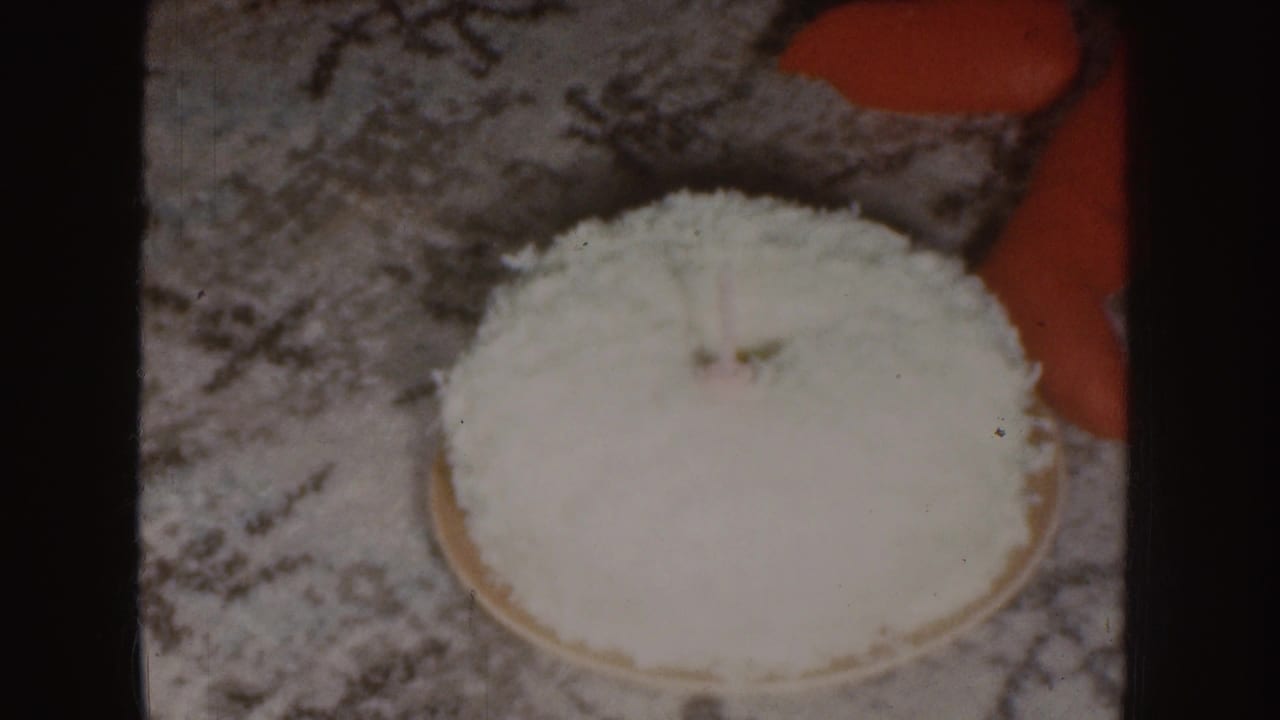 Round coconut-covered cake on patterned carpet beside a child's red clothing.