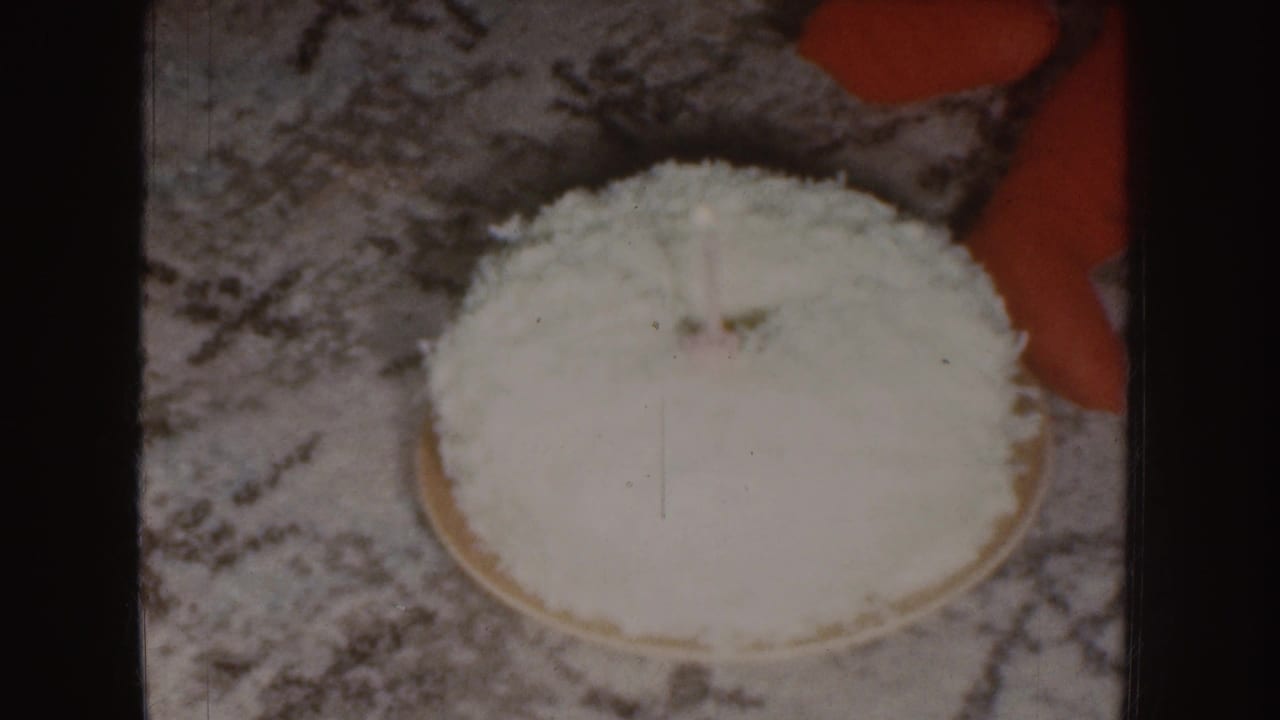 Coconut-covered cake centered on a patterned carpet with red clothing at the edge.