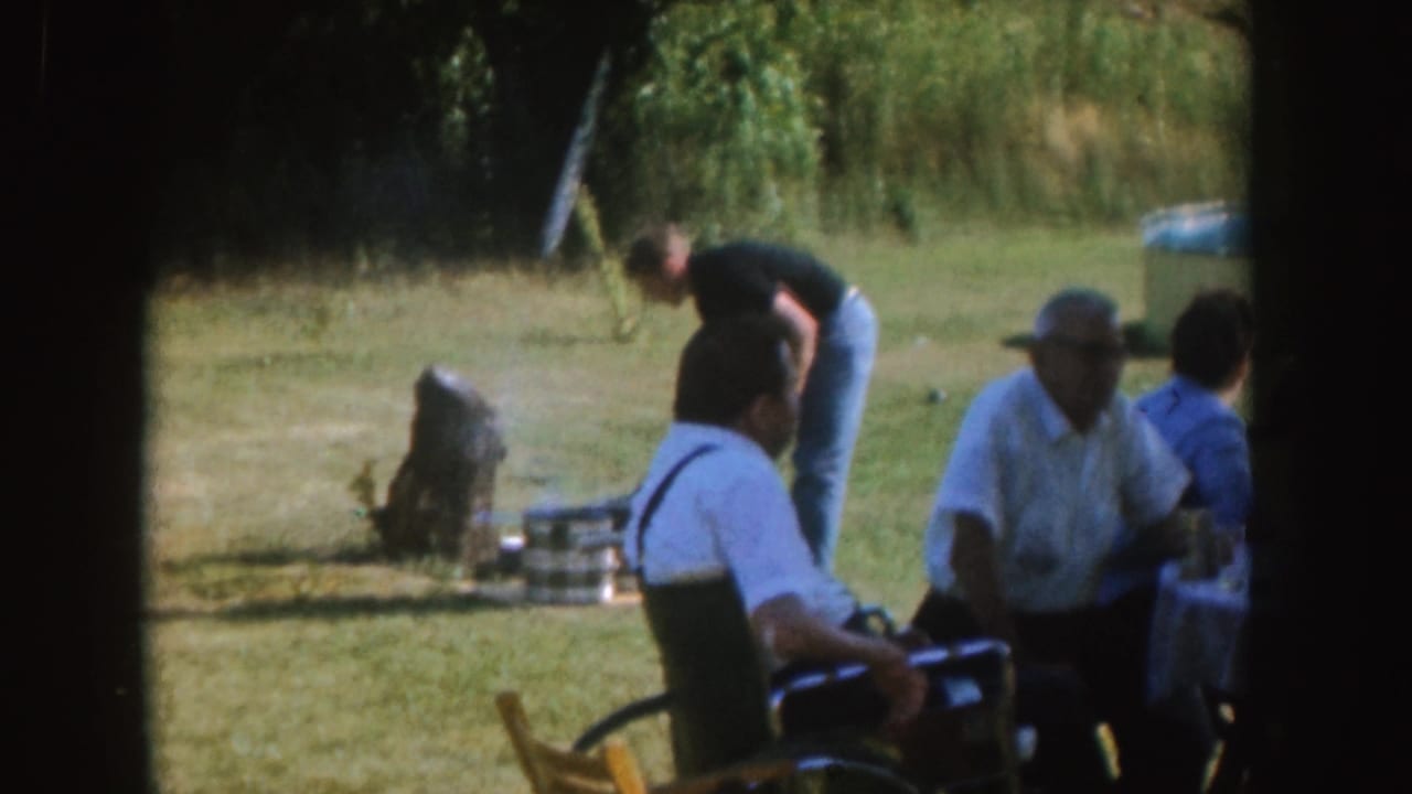 A man tends a grill while adults sit near an outdoor table.