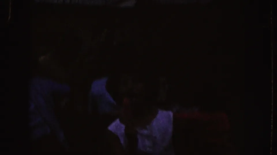 Nebraska 1955 frame with seated viewers in a low-lit room, faces partly obscured by shadow and projector light.