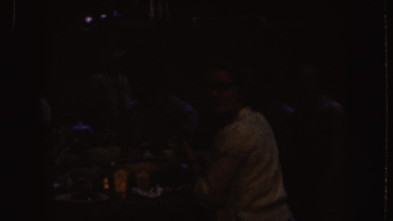 Dim indoor table scene with adults seated in shadow and glasses on the table.