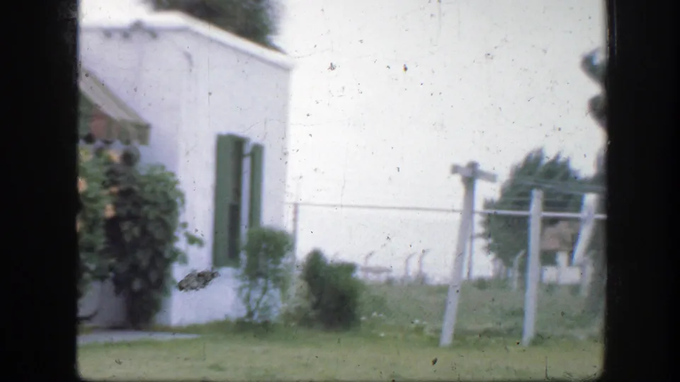 1945 Florida backyard view showing a white house side, green shutters, low shrubs, grass, and an empty clothesline structure.