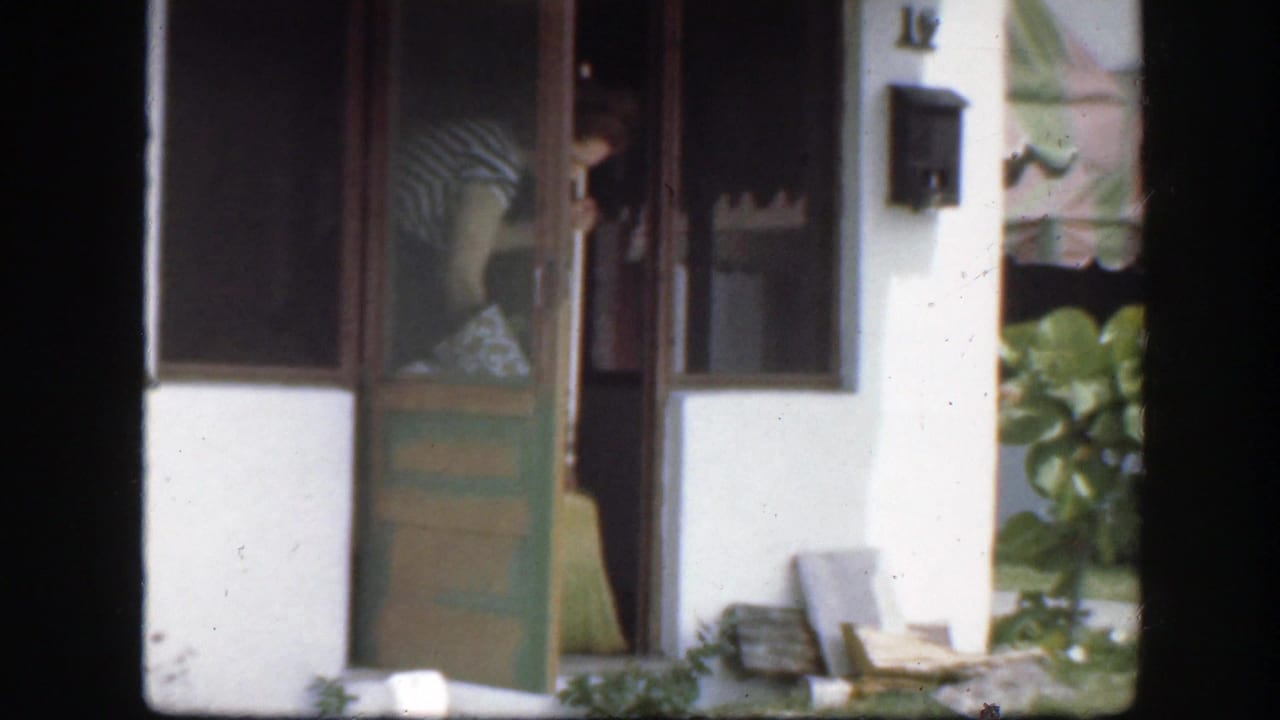 Woman in striped dress bends near a green doorway with a broom inside the entrance.