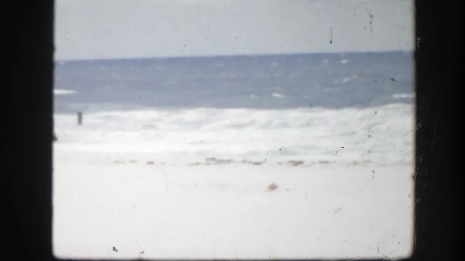 1945 Florida shoreline frame with white surf rolling toward a mostly empty stretch of sand.