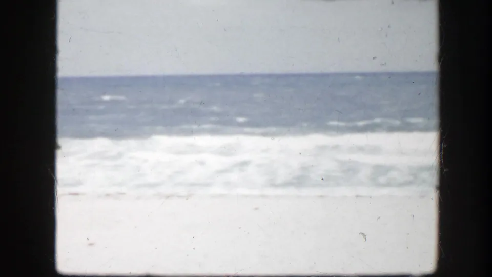 Florida beach home-movie frame showing soft, washed surf and open sand with no visible people.