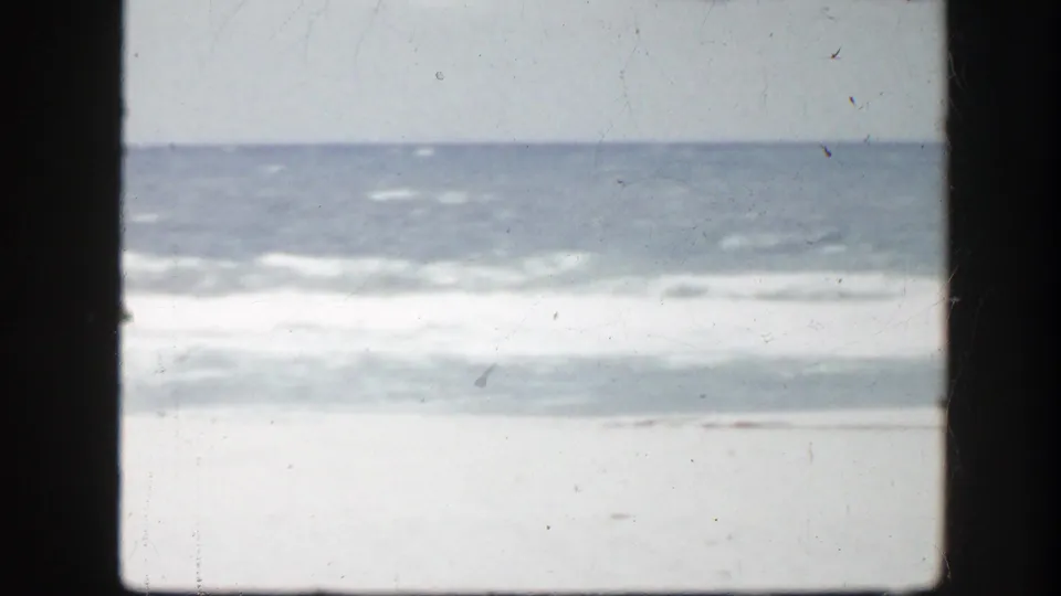 1945 Florida coastal frame with a low horizon, foamy waves, pale sand, and visible film wear.
