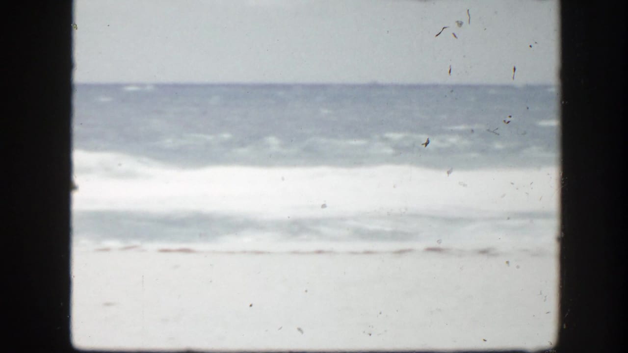 1940s Florida beach view with surf and sand framed by a dark vertical window or doorway edge.
