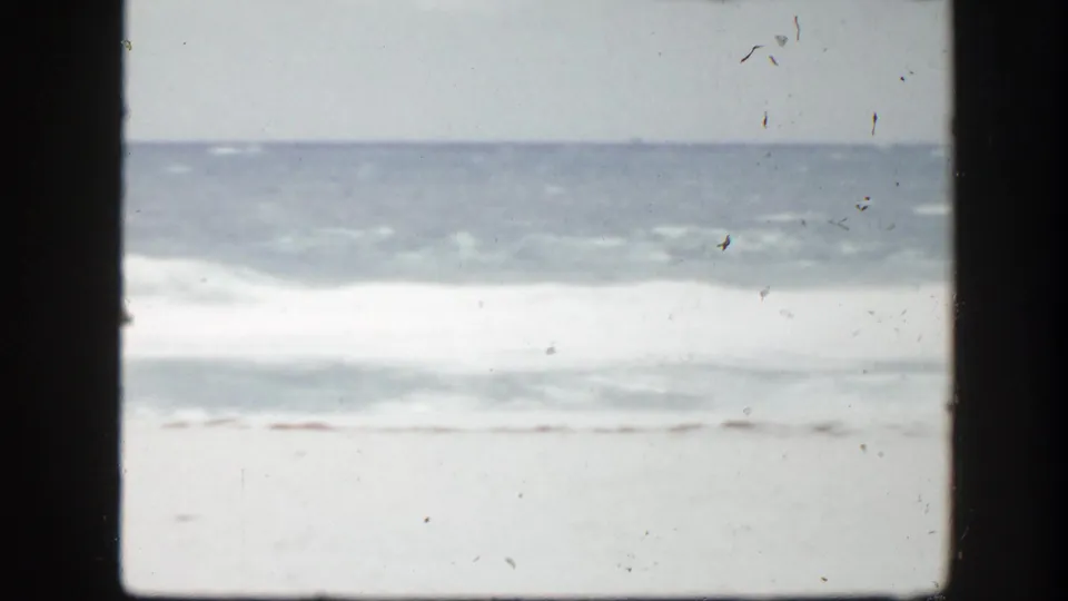 1940s Florida beach view with surf and sand framed by a dark vertical window or doorway edge.