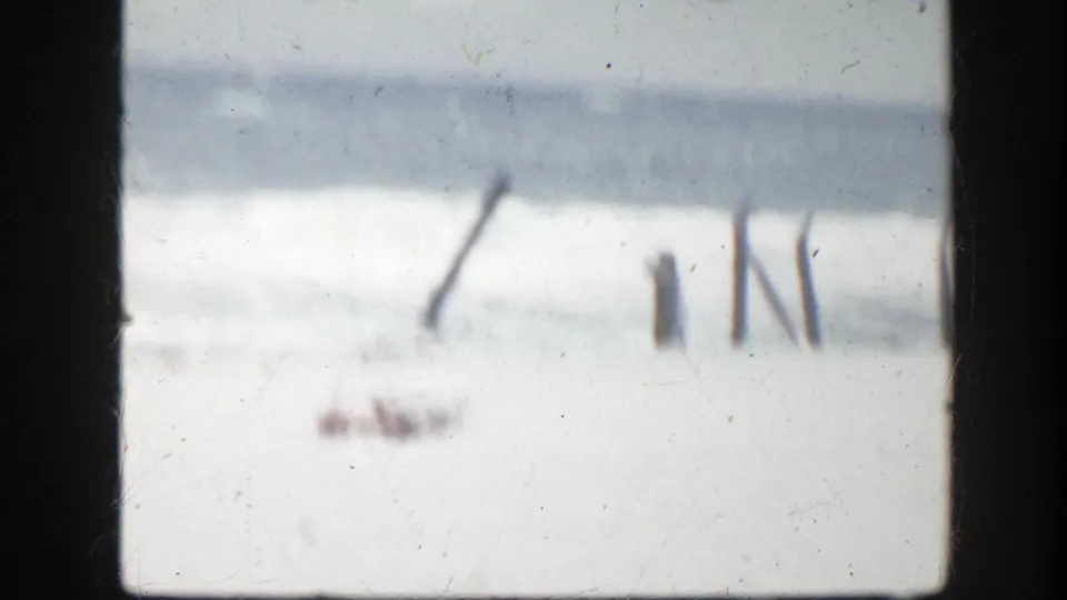 Soft 1940s Florida beach view with breaking surf and indistinct poles or beach markers in the foreground.