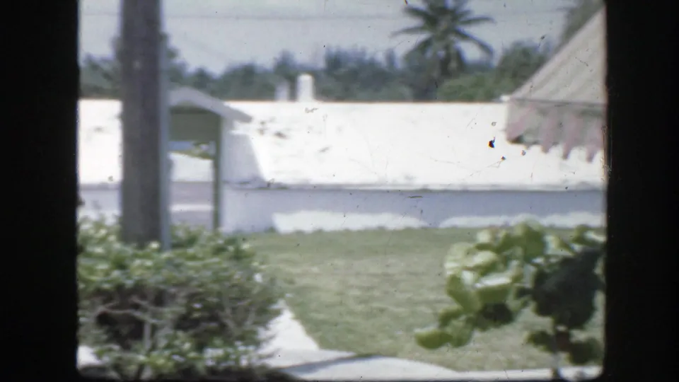 Florida resort or residential area with white low buildings, palms, trimmed grass, shrubs, and a sidewalk.