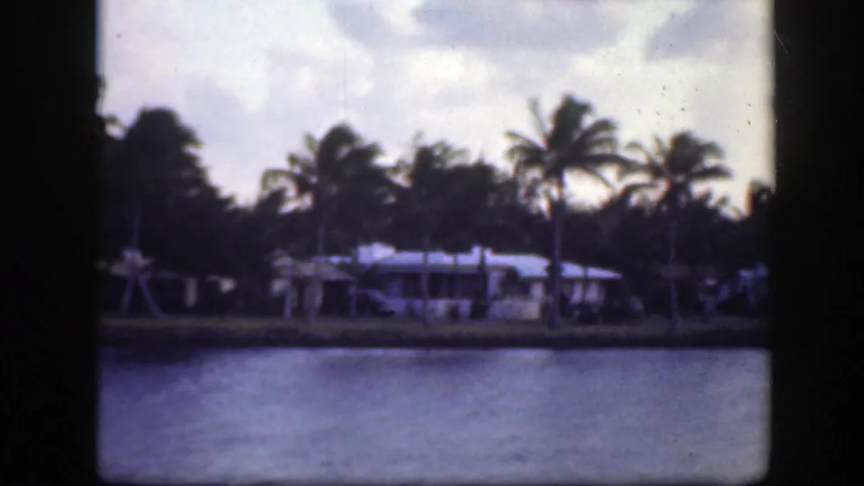 1945 Florida home-movie frame with darker exposure on palm trees, low waterfront houses, and water.