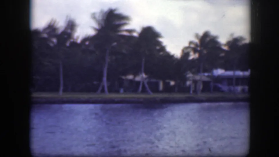 End of a 1945 Florida 8mm pan showing palms, low buildings, and rippled water under a cloudy sky.