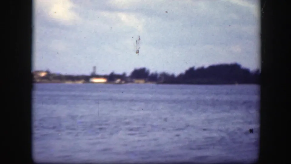 1945 Florida 8mm frame looking across blue water toward a distant low shoreline and dark trees under cloud cover.
