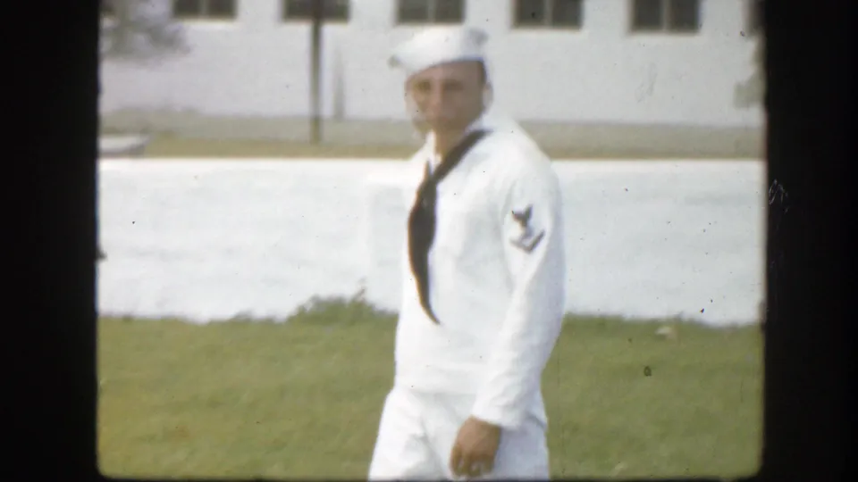 Adult sailor in a white uniform and cap walks across a Florida lawn in 1945 home-movie footage.