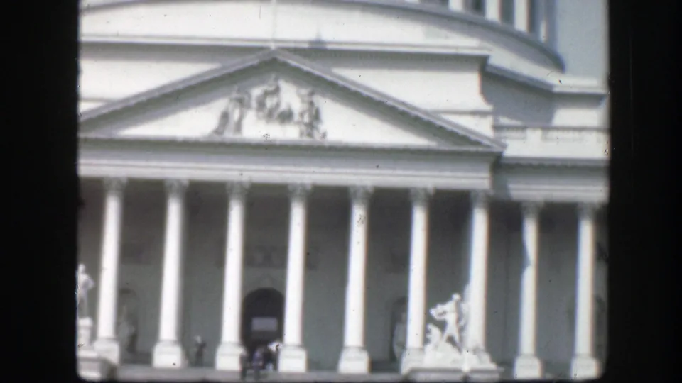 1945 Washington, D.C. home-movie frame of the U.S. Capitol facade, showing columns, pediment, dome base, and a statue at right.